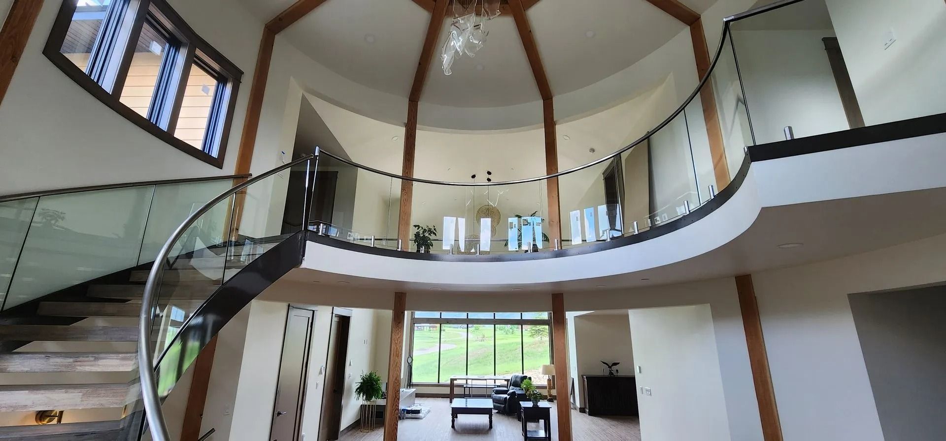Spacious interior with spiral staircase, balcony, and large windows overlooking greenery.