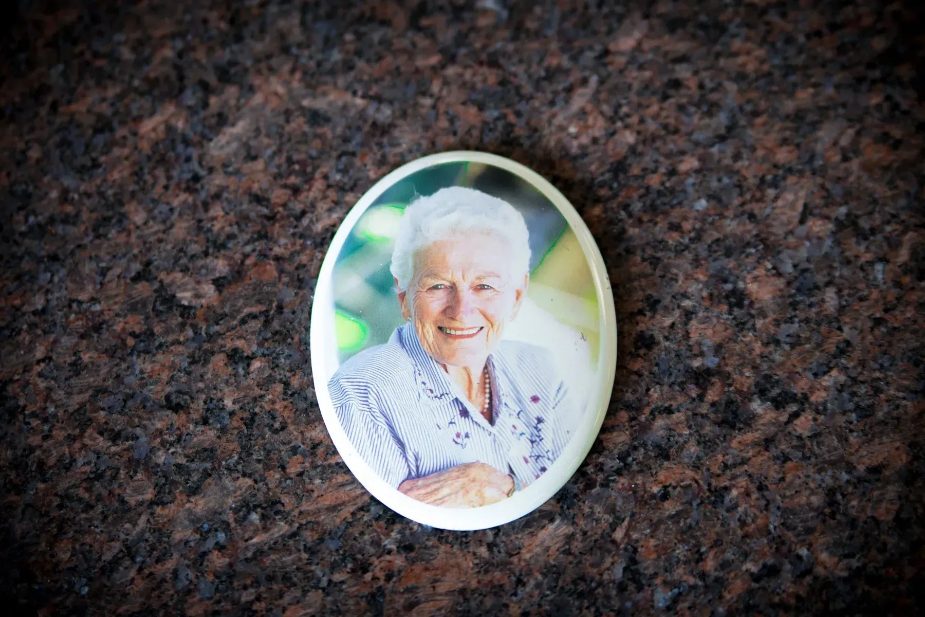 Oval memorial portrait on a dark granite headstone, showing a smiling person in a white shirt.