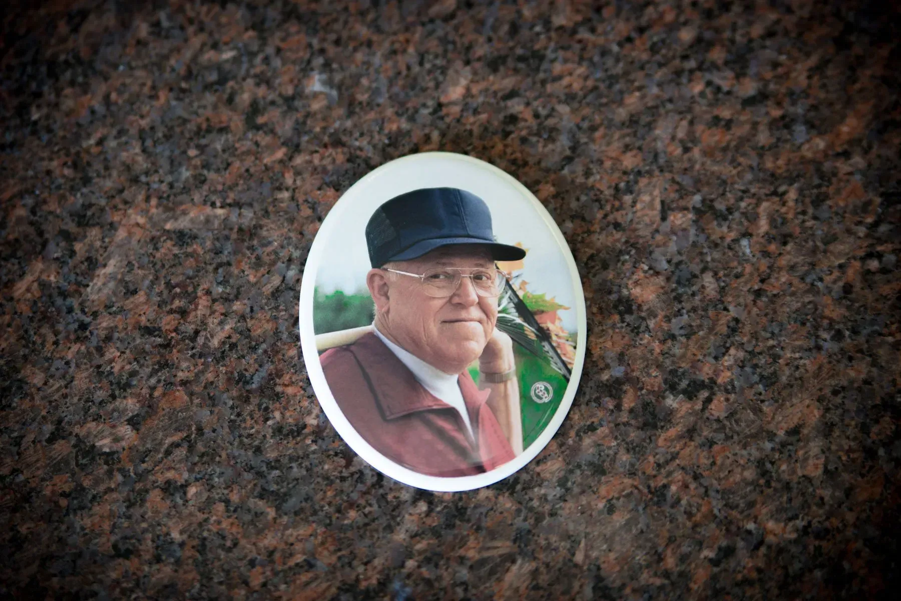 Oval portrait photo on dark granite plaque of a man in a flat cap and maroon jacket