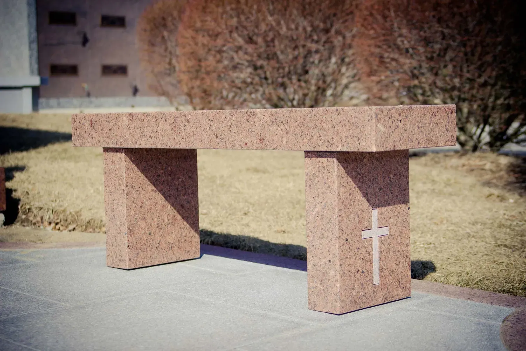 Granite memorial bench with white cross in a landscaped outdoor area