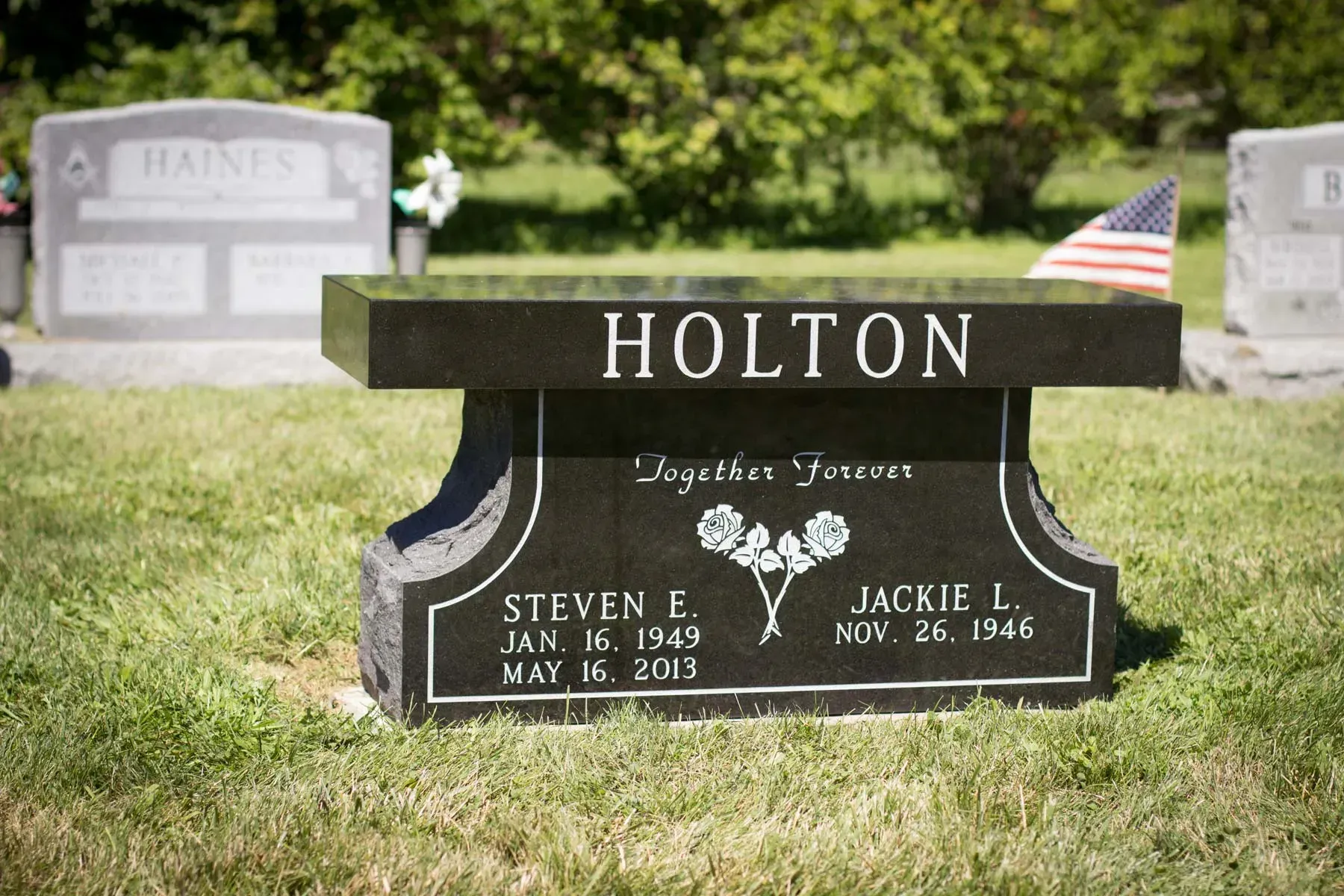 Holton gravestone in a grassy cemetery, with an American flag in the background.