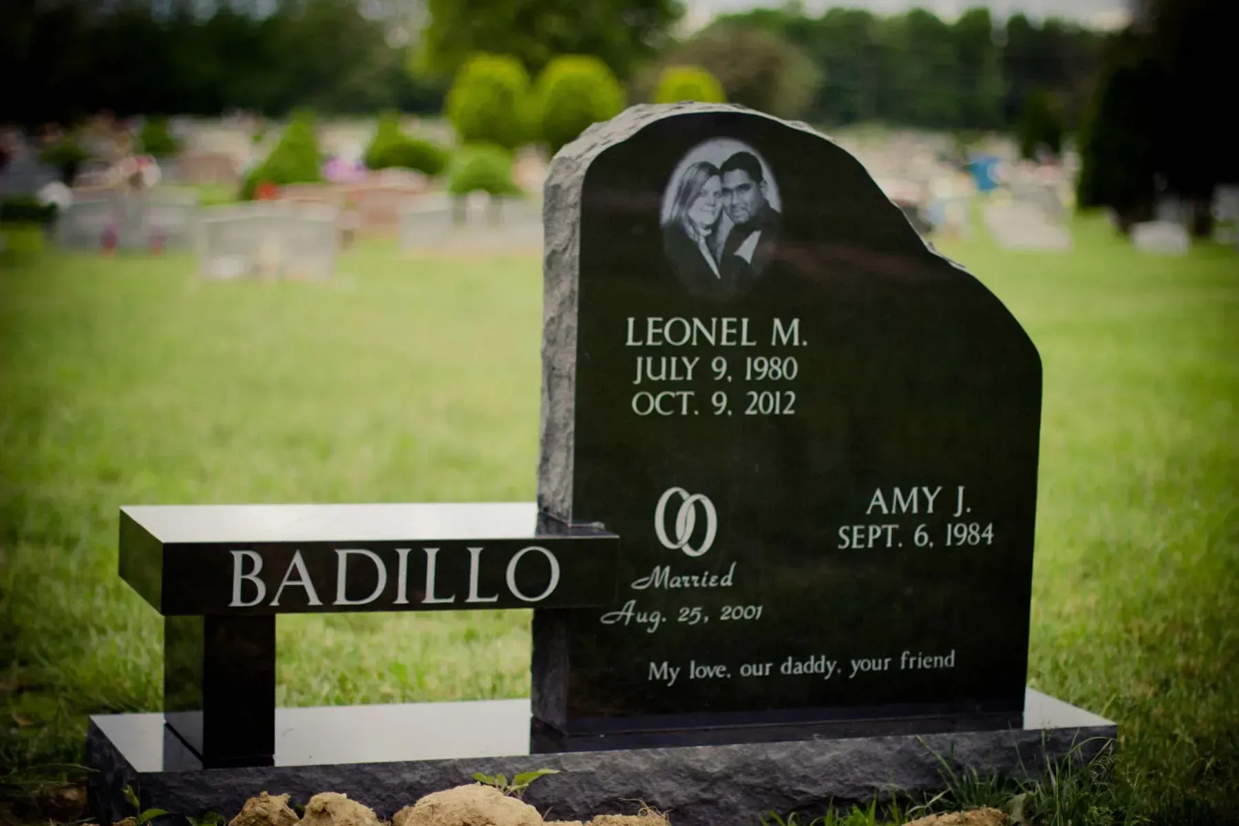 Black memorial headstone and bench in a cemetery with the name BADILLO engraved on the front