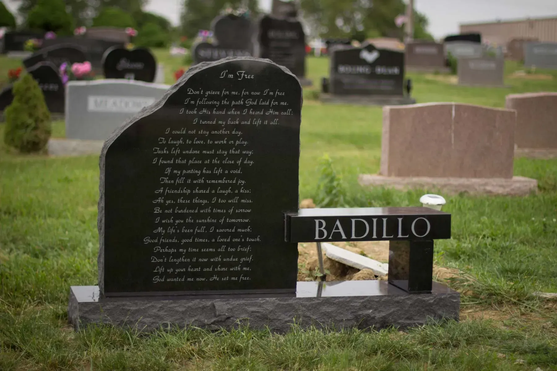 Black gravestone in a cemetery with the name BADILLO on a small plaque
