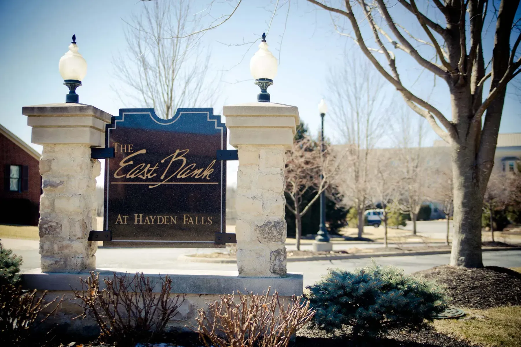 Stone entrance sign for East Park at Hayden Hills beside trees and landscaping under a clear sky