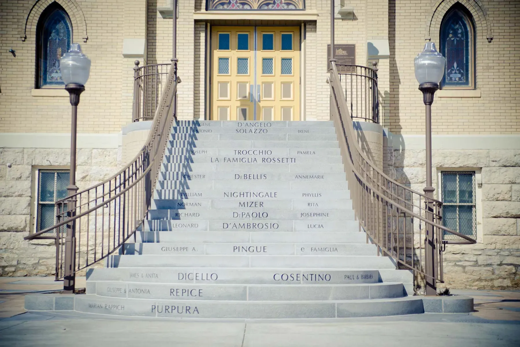 Stone steps leading to a yellow double door, flanked by brick walls and metal railings under street lamps