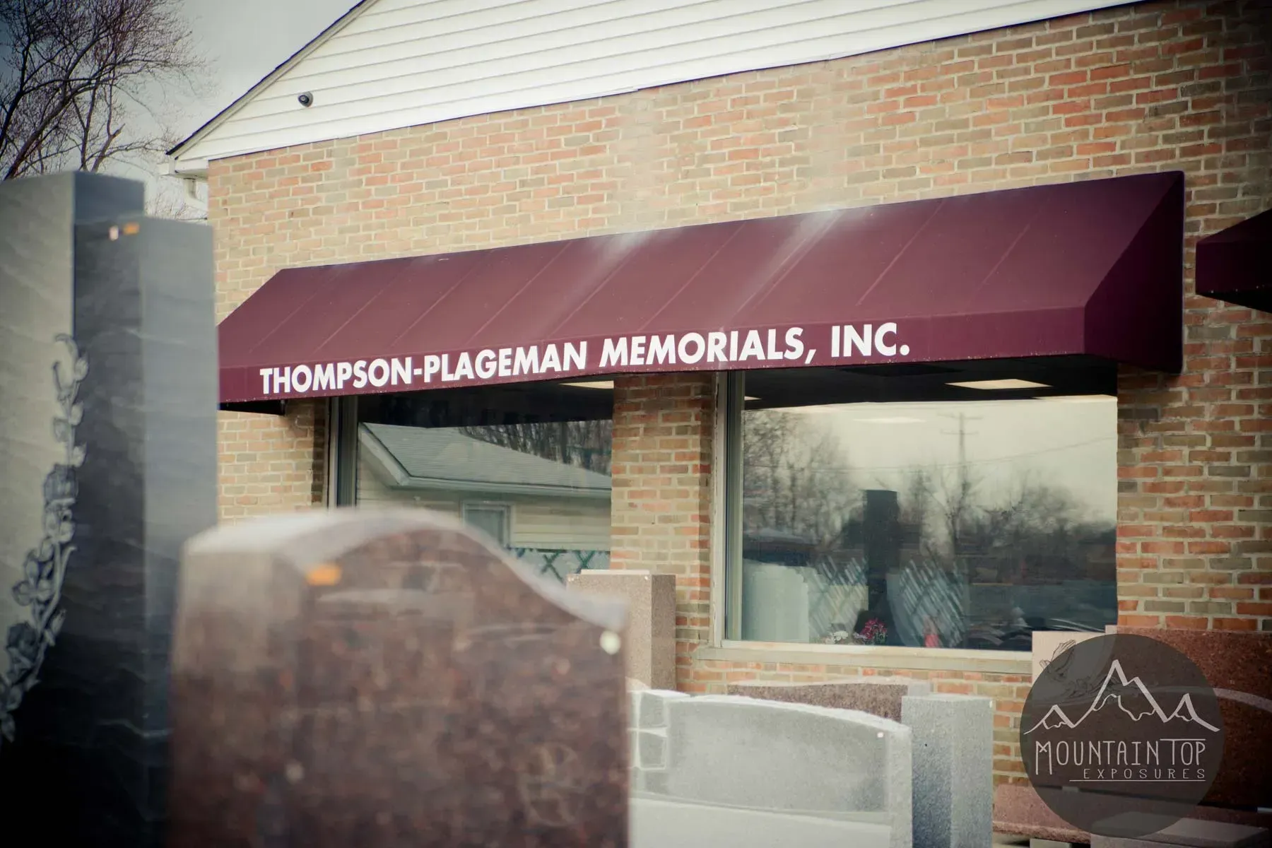 Thompson-Plageman Memorials storefront with maroon awning and a stone monument display outside