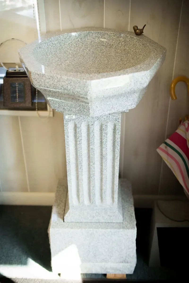 White pedestal or planter on a shelf, with a textured top and fluted column base.