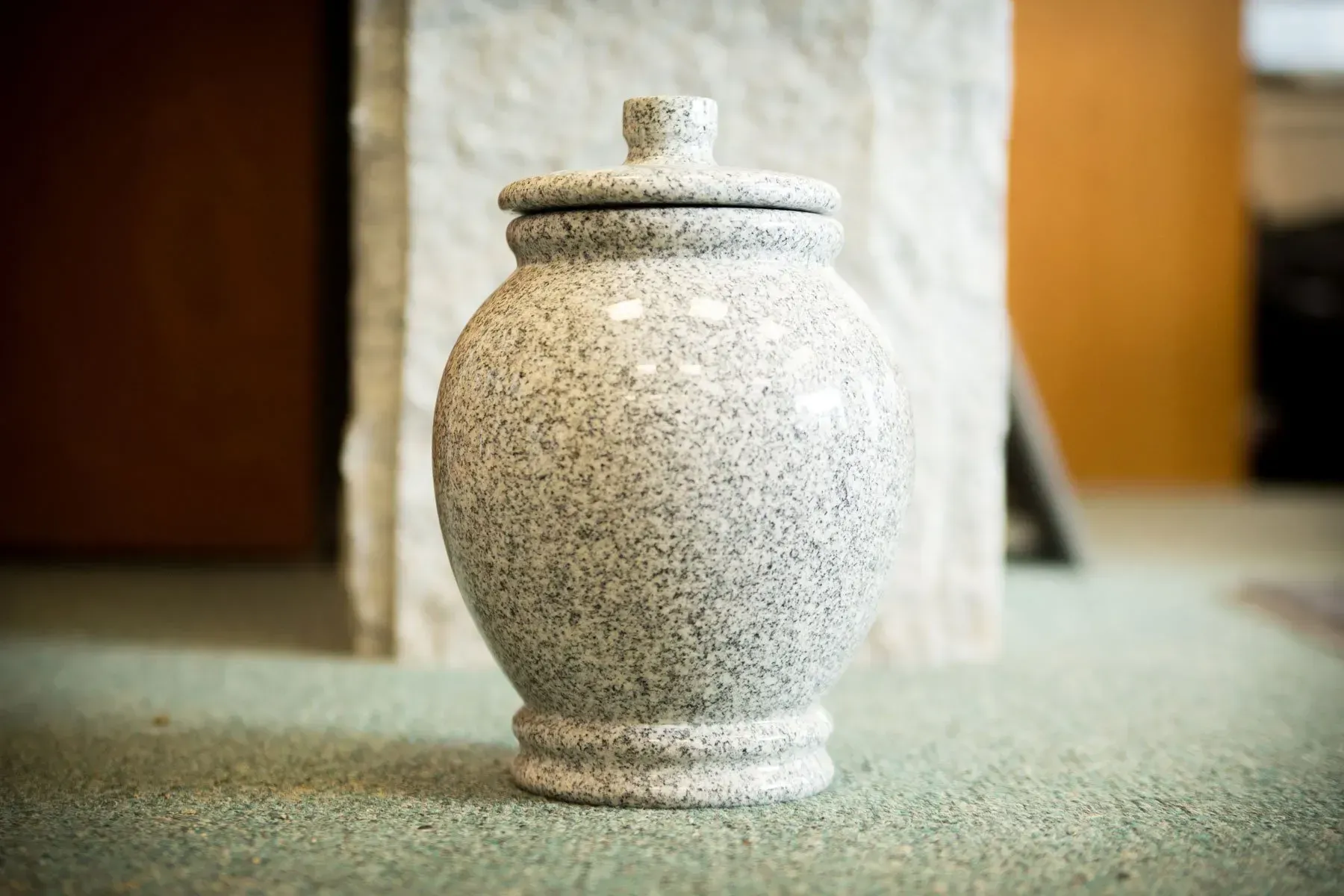 Speckled ceramic urn with lid on a carpeted floor indoors