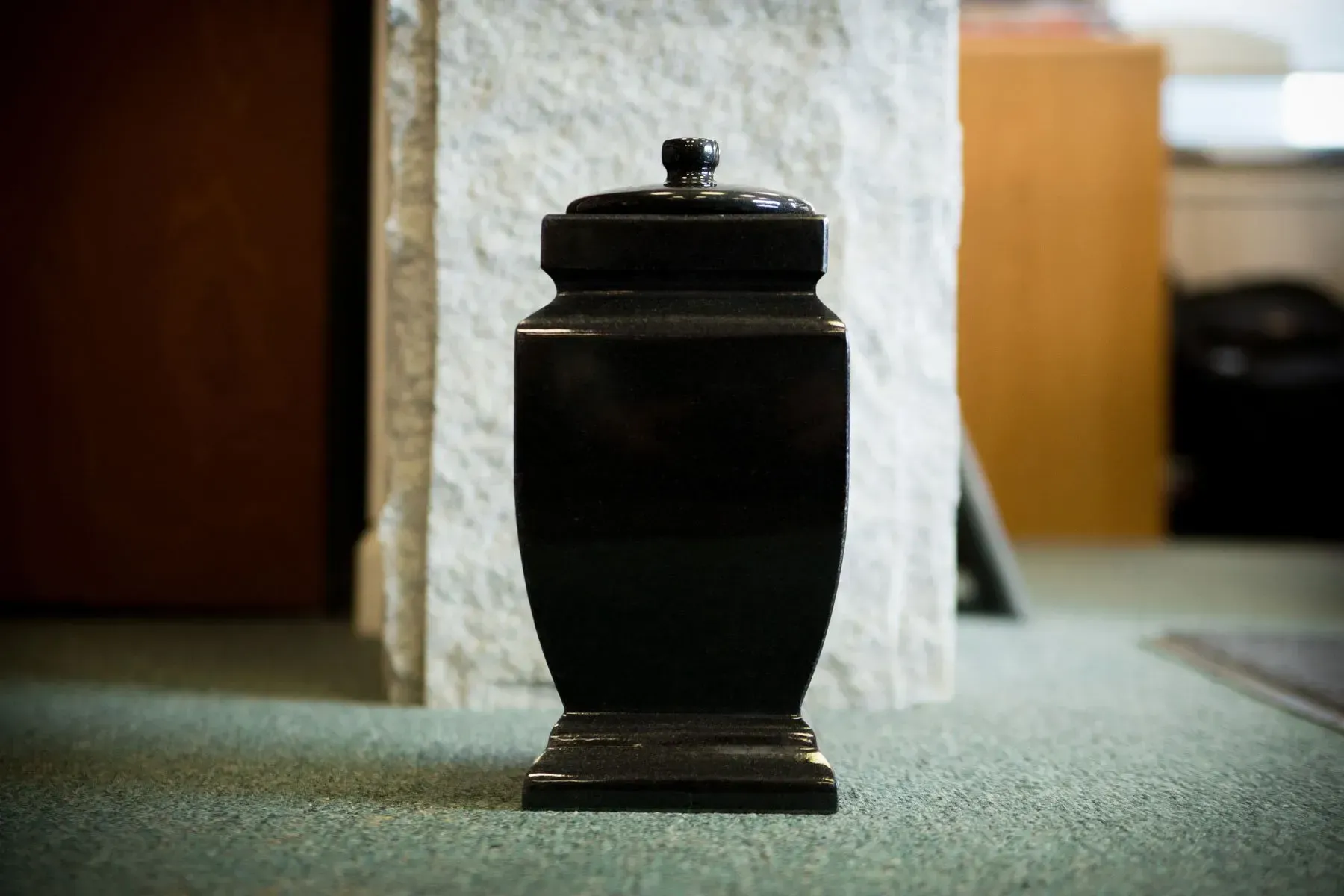 Black urn with lid on a carpeted floor in a room
