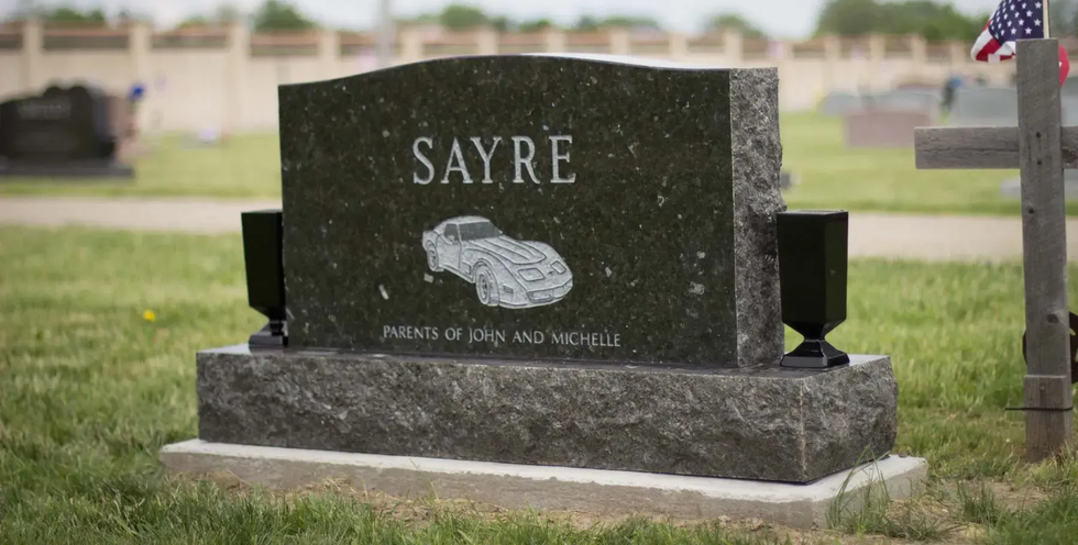 Gravestone marked “SAYRE” in a cemetery, with a small American flag nearby.