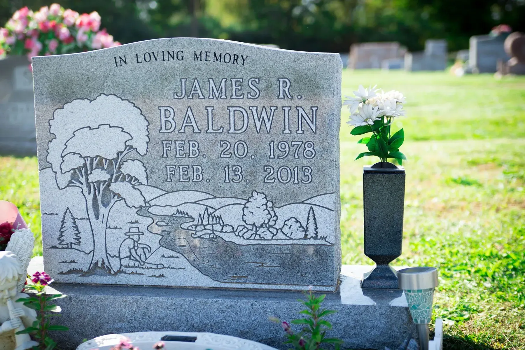 Gravestone with engraved tree and flowers in a cemetery, marked in loving memory of James R. Baldwin.