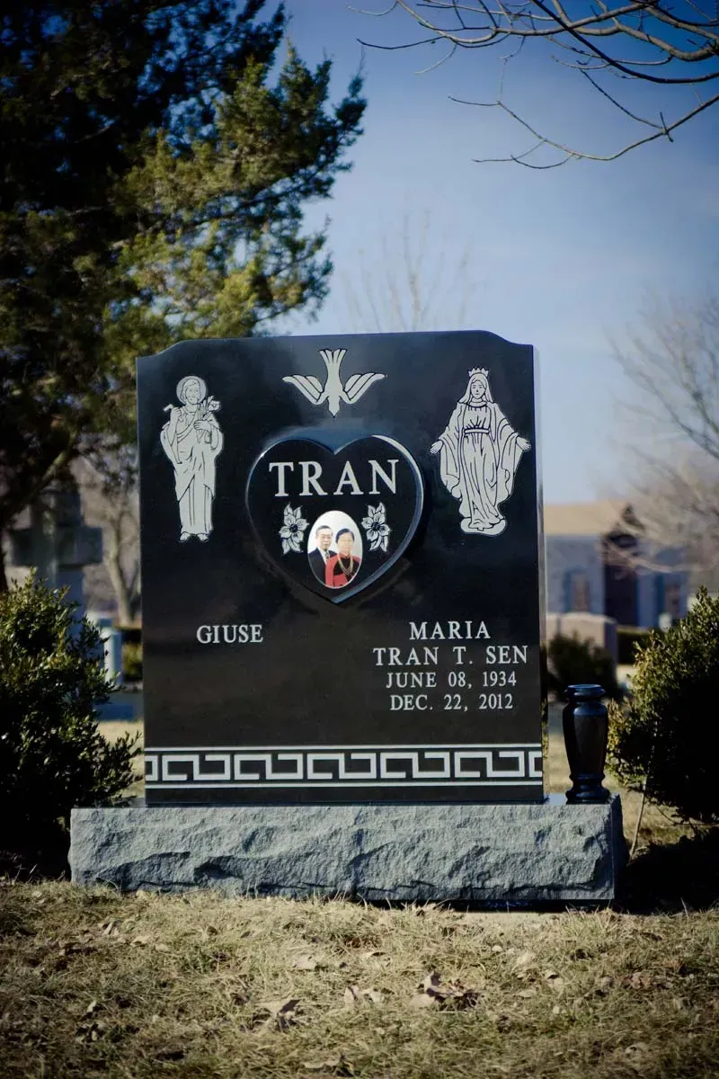Black granite memorial headstone with “TRAN” and floral engravings in a cemetery