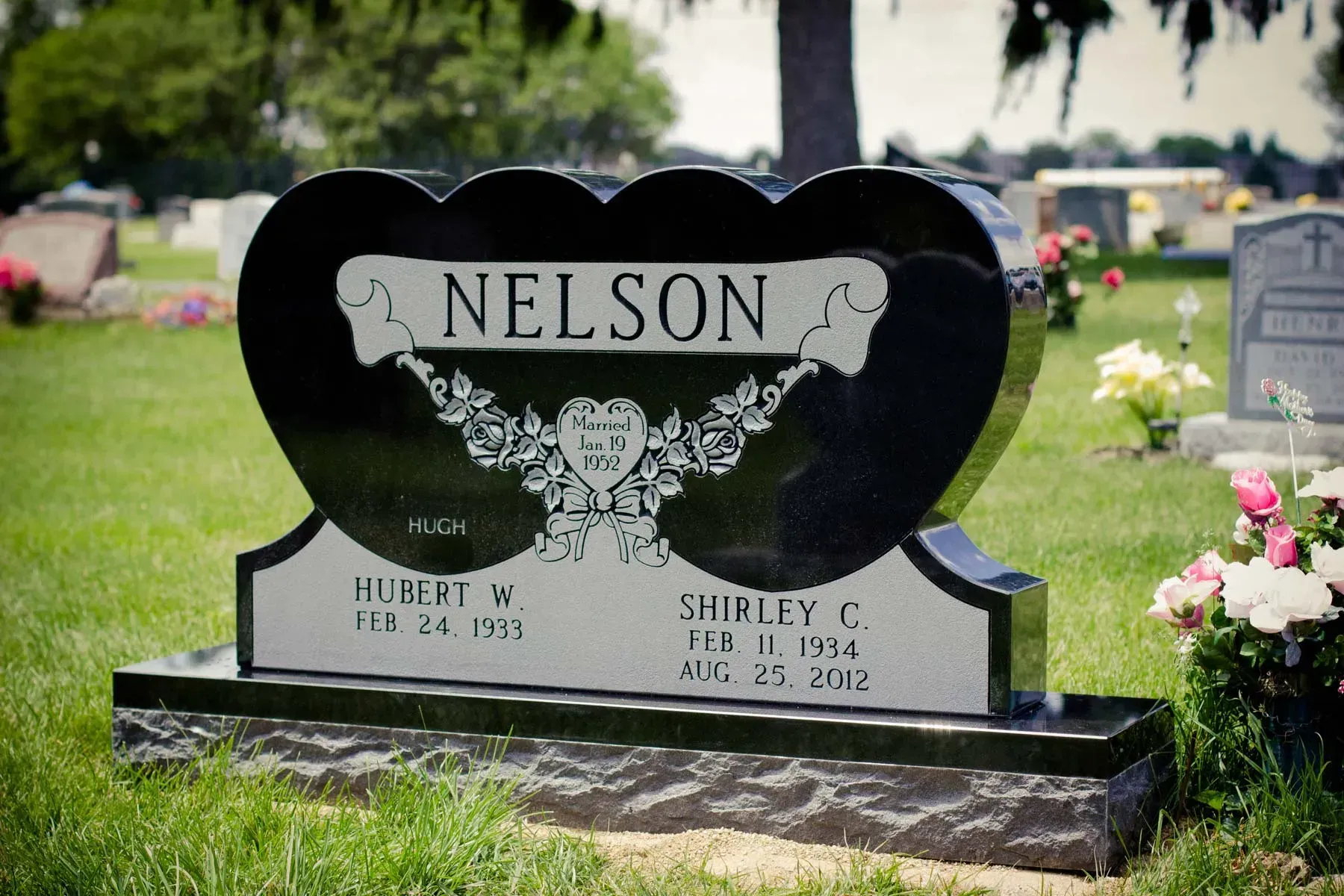 Black Nelson gravestone with engraved names and flowers in a cemetery