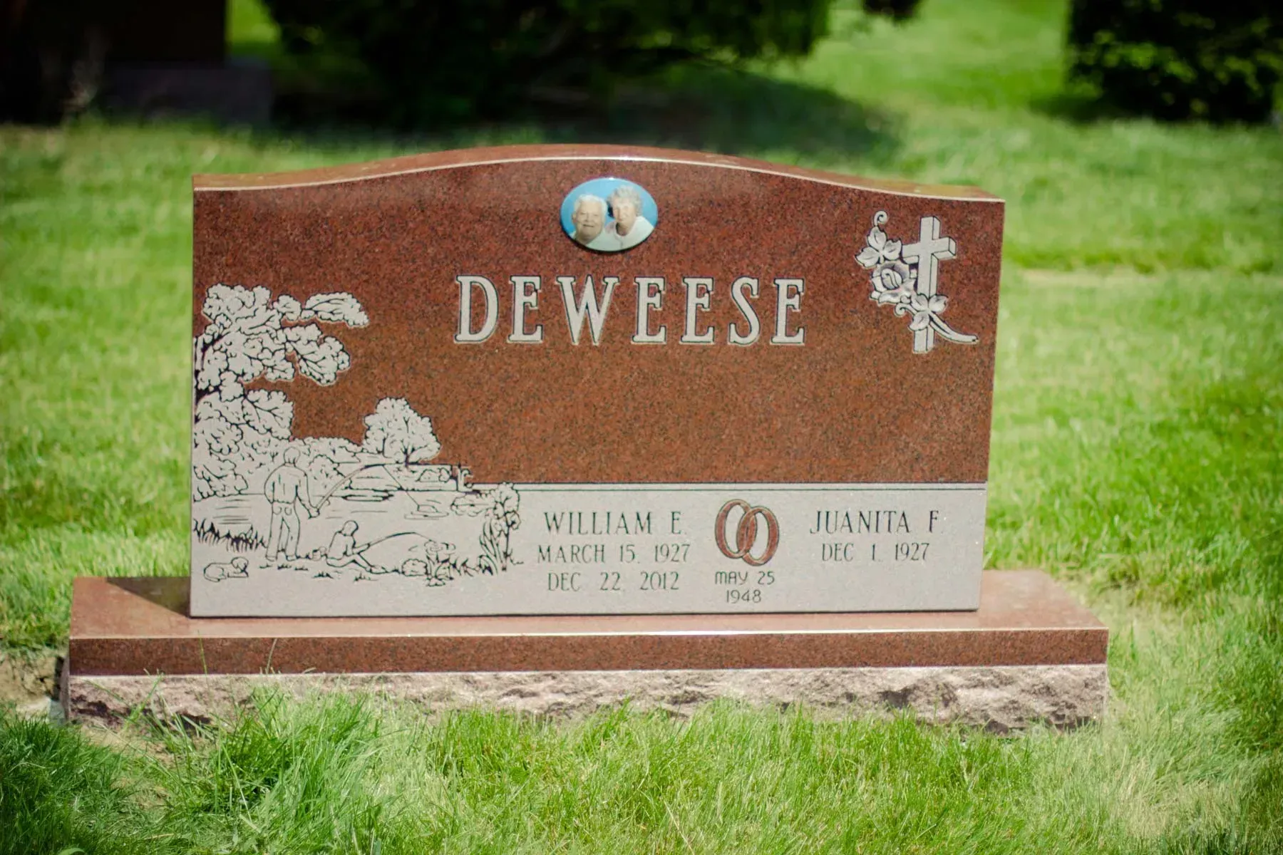 Brown granite gravestone with floral carvings reading “DEWESE,” set in green grass