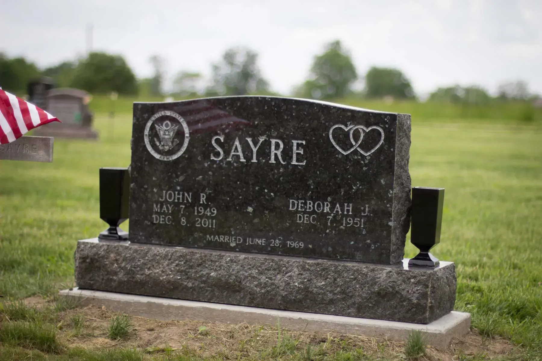 Black granite Sayre gravestone in a grassy cemetery with an American flag on the left