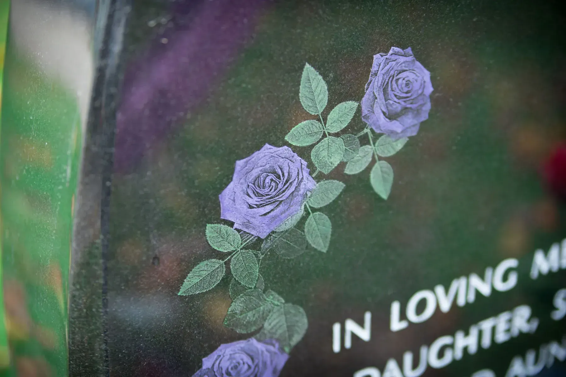 Purple roses on a dark memorial plaque with partially visible “In Loving Memory” text