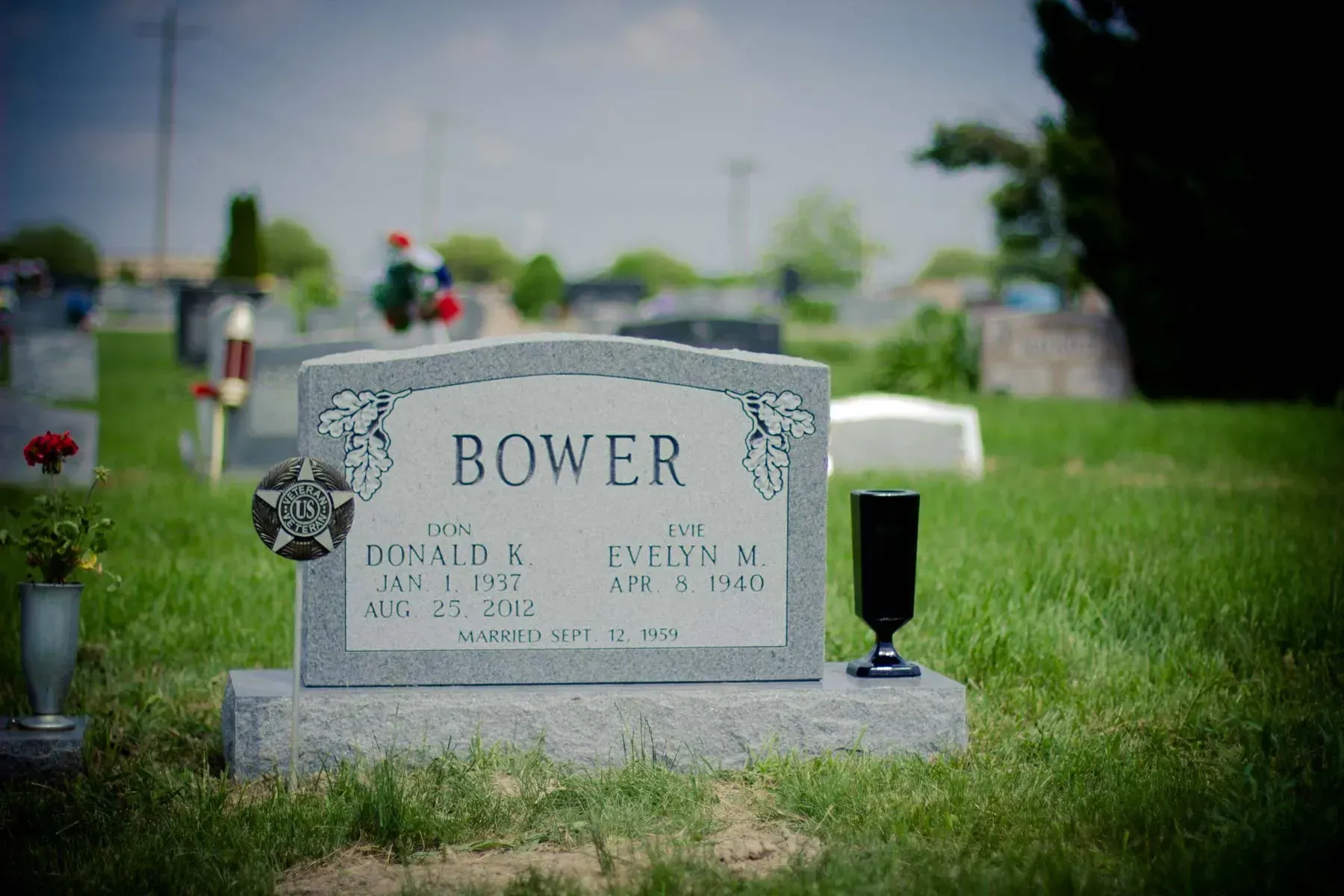 Bower gravestone in a green cemetery, with blurred headstones in the background.