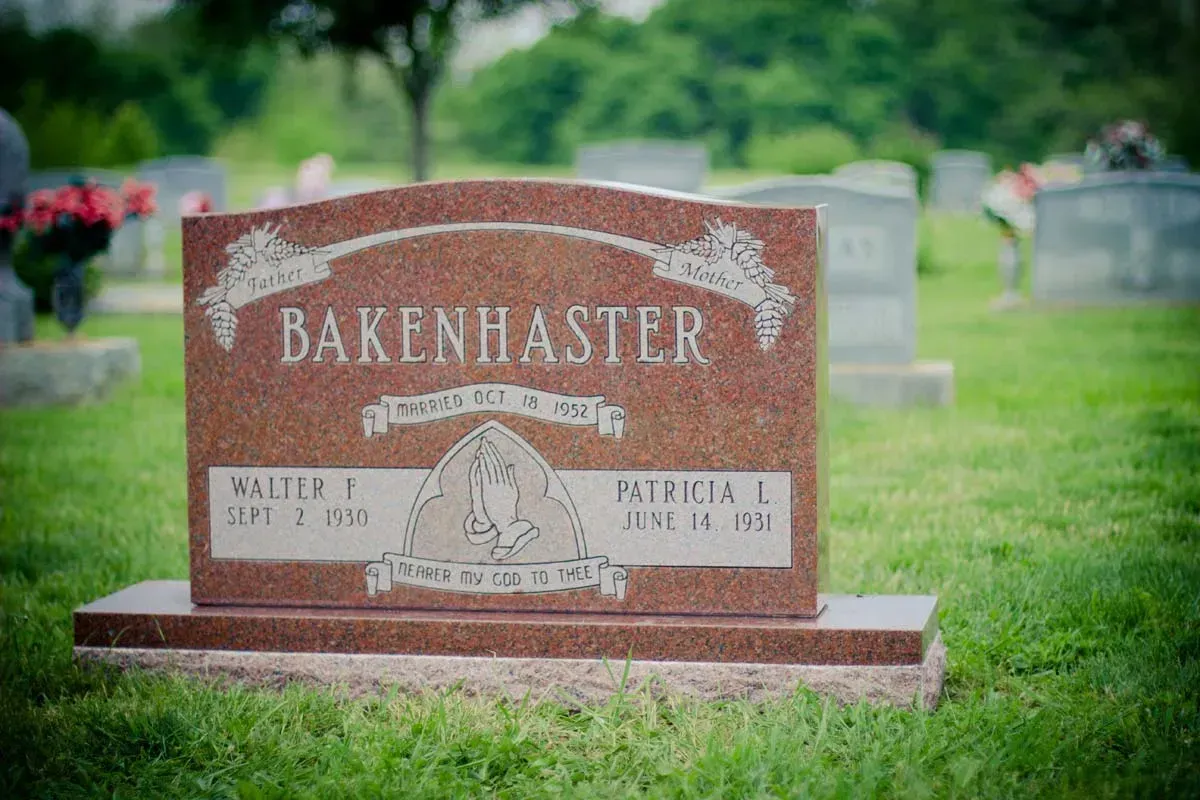 Brown Bakenhaster gravestone in a green cemetery, engraved with a cross and floral design