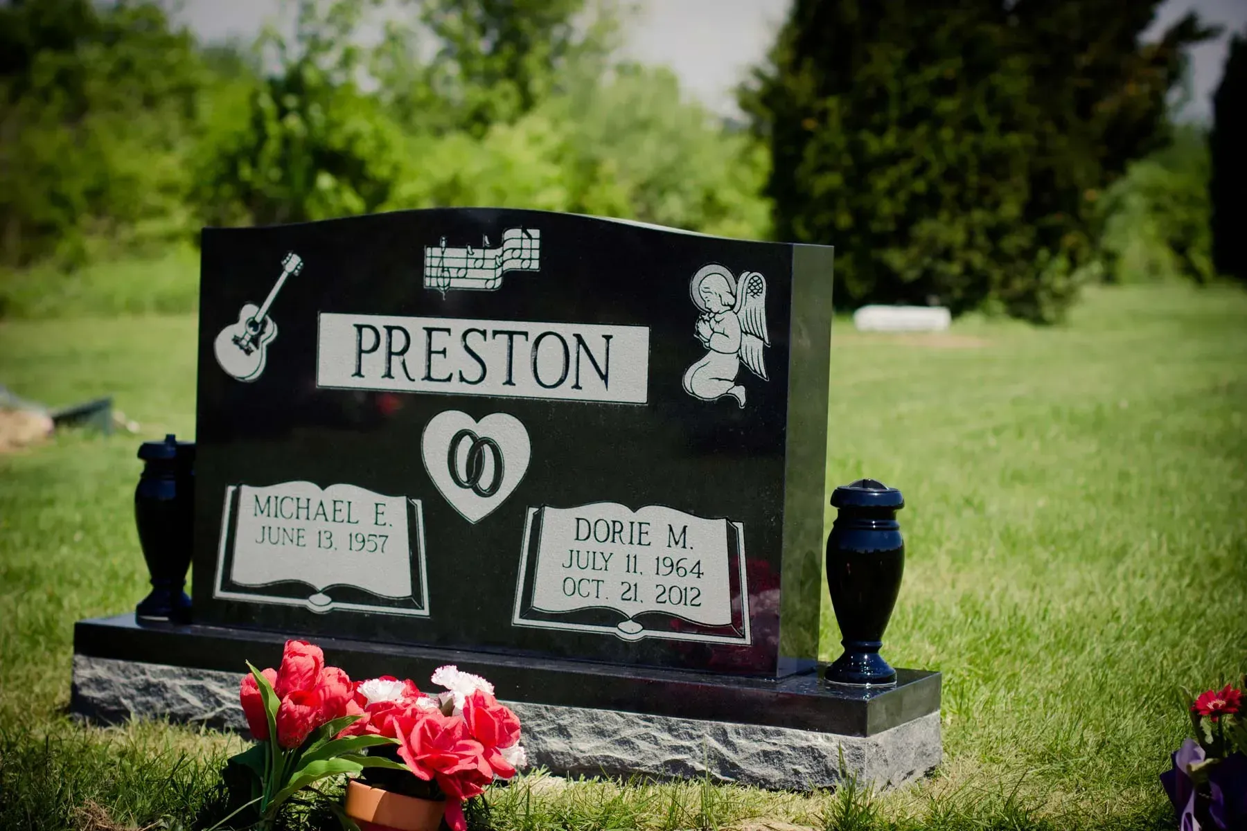Black memorial gravestone with “PRESTON” and red flowers in a grassy cemetery￼
