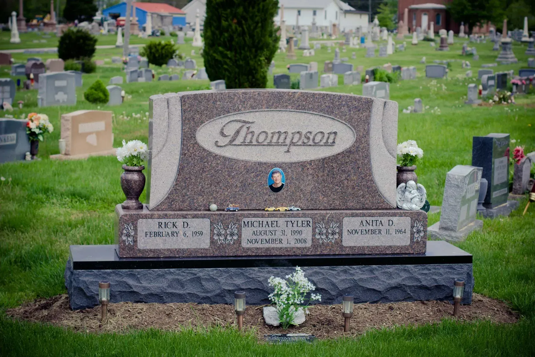 Thompson family gravestone in a cemetery with flowers and nearby headstones