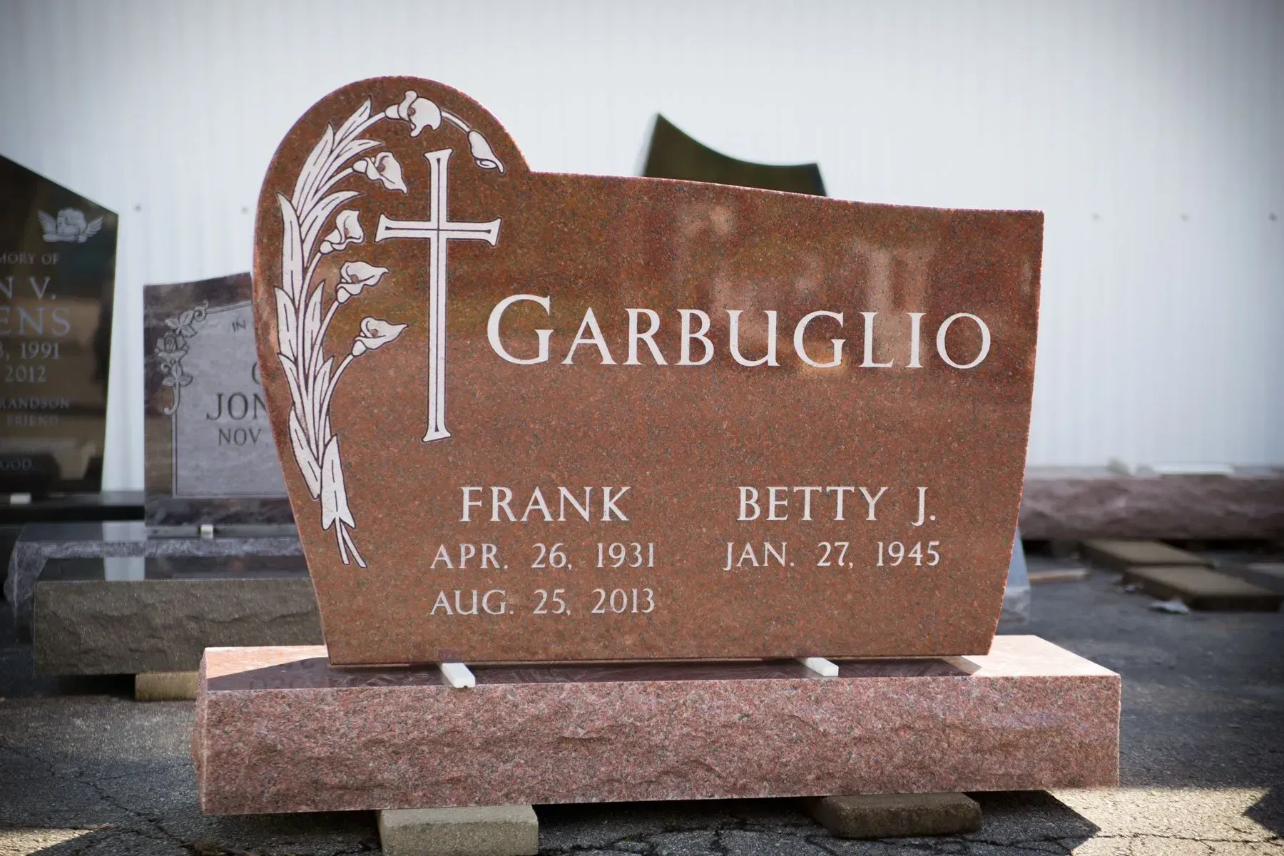 Brown granite gravestone engraved “Garbiglio” with white cross and floral design in a cemetery