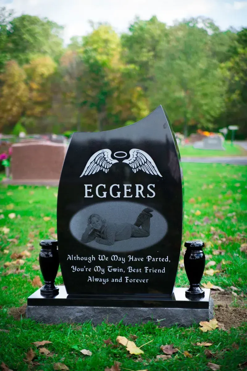 Black Egger family gravestone with angel wings in a green cemetery setting