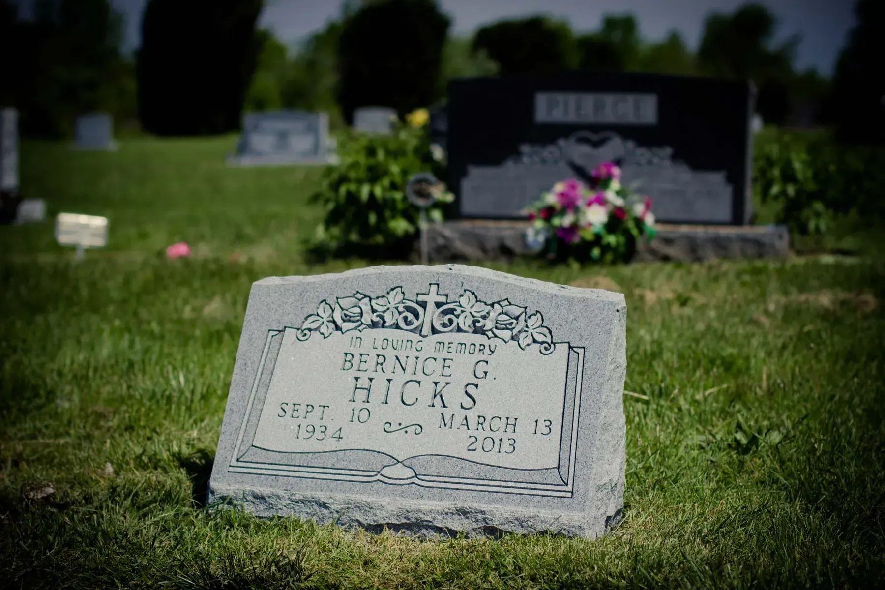 Gravestone in a cemetery with a bouquet of pink flowers in the background.