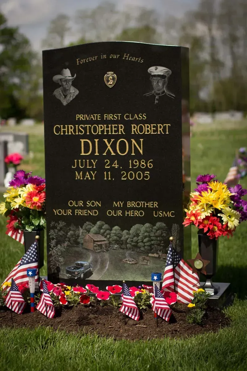 Black gravestone with flowers and small American flags in a cemetery