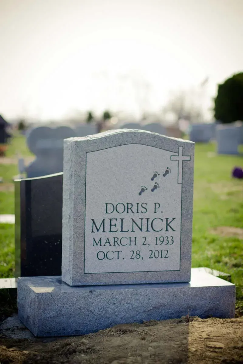 Gray gravestone in a cemetery with a cross and the name Doris P. Melnick.