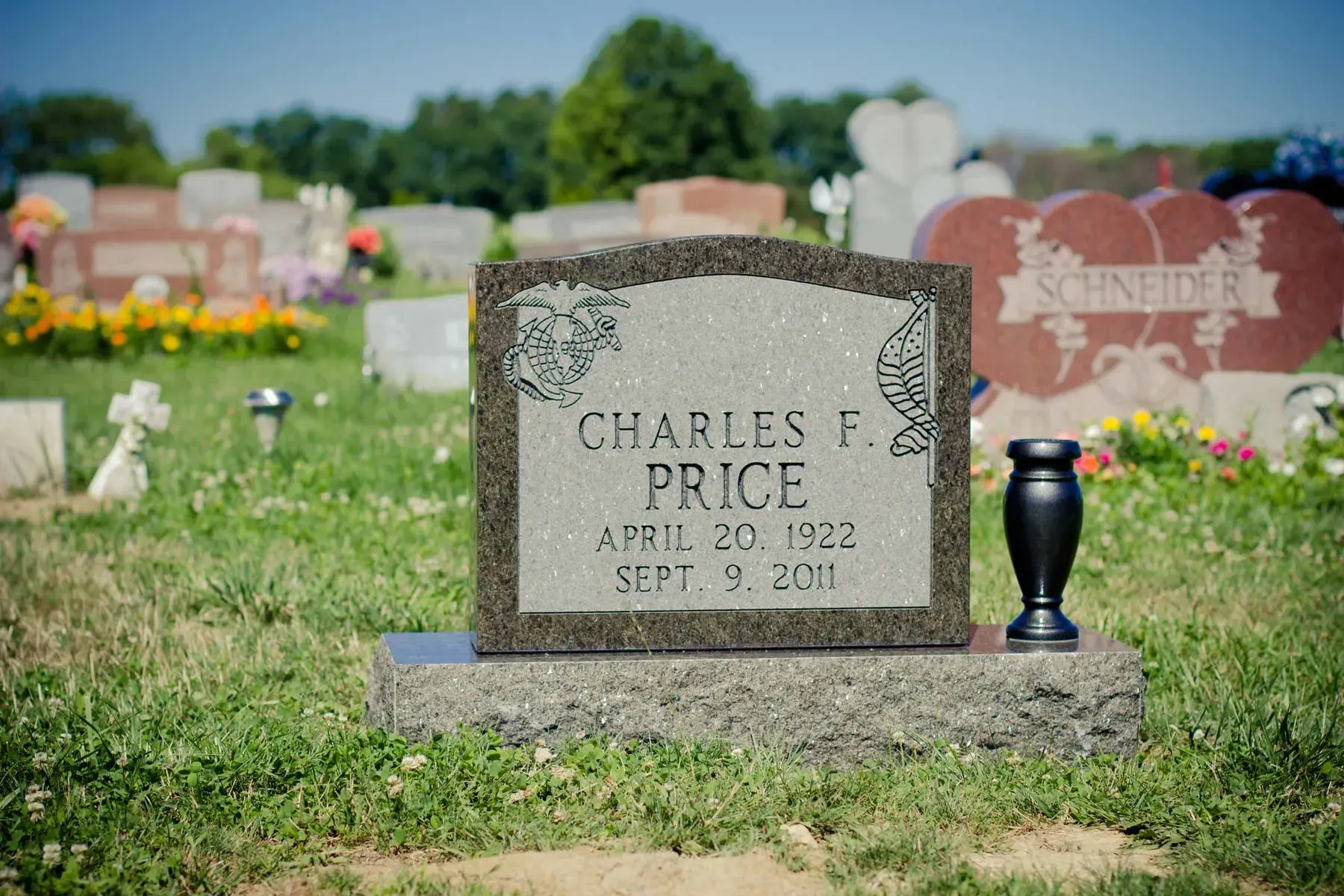 Gravestone for Charles Price in a cemetery, with flowers and other headstones in the background.