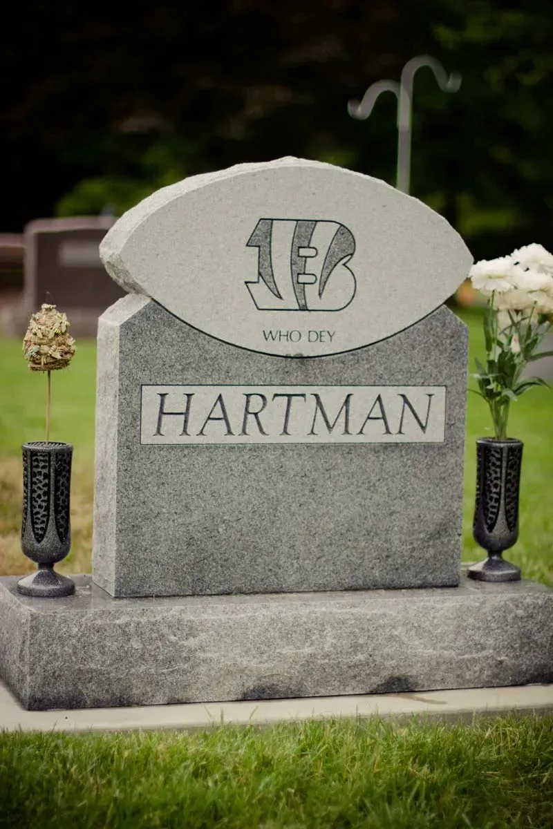 Hartman gravestone with engraved emblem and two black vases in a cemetery garden