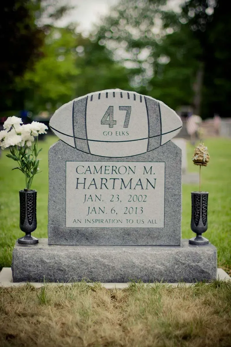 Memorial gravestone with football number 47 in a grassy cemetery, flanked by white flowers and black vases