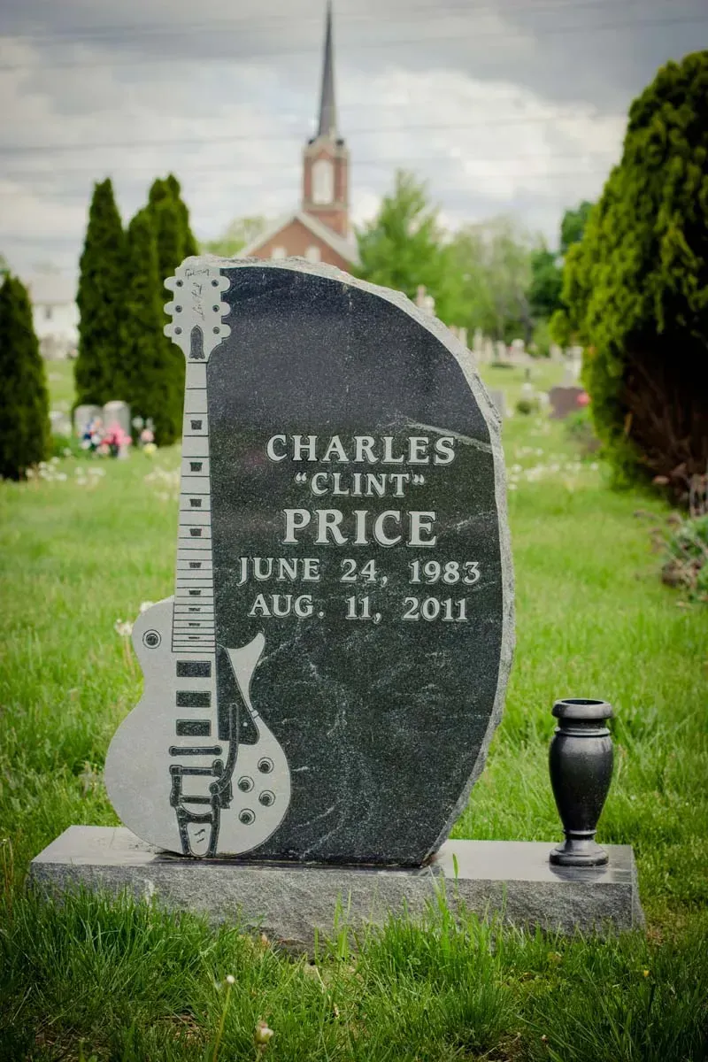 Gravestone for Charles Price with guitar carving in a green cemetery