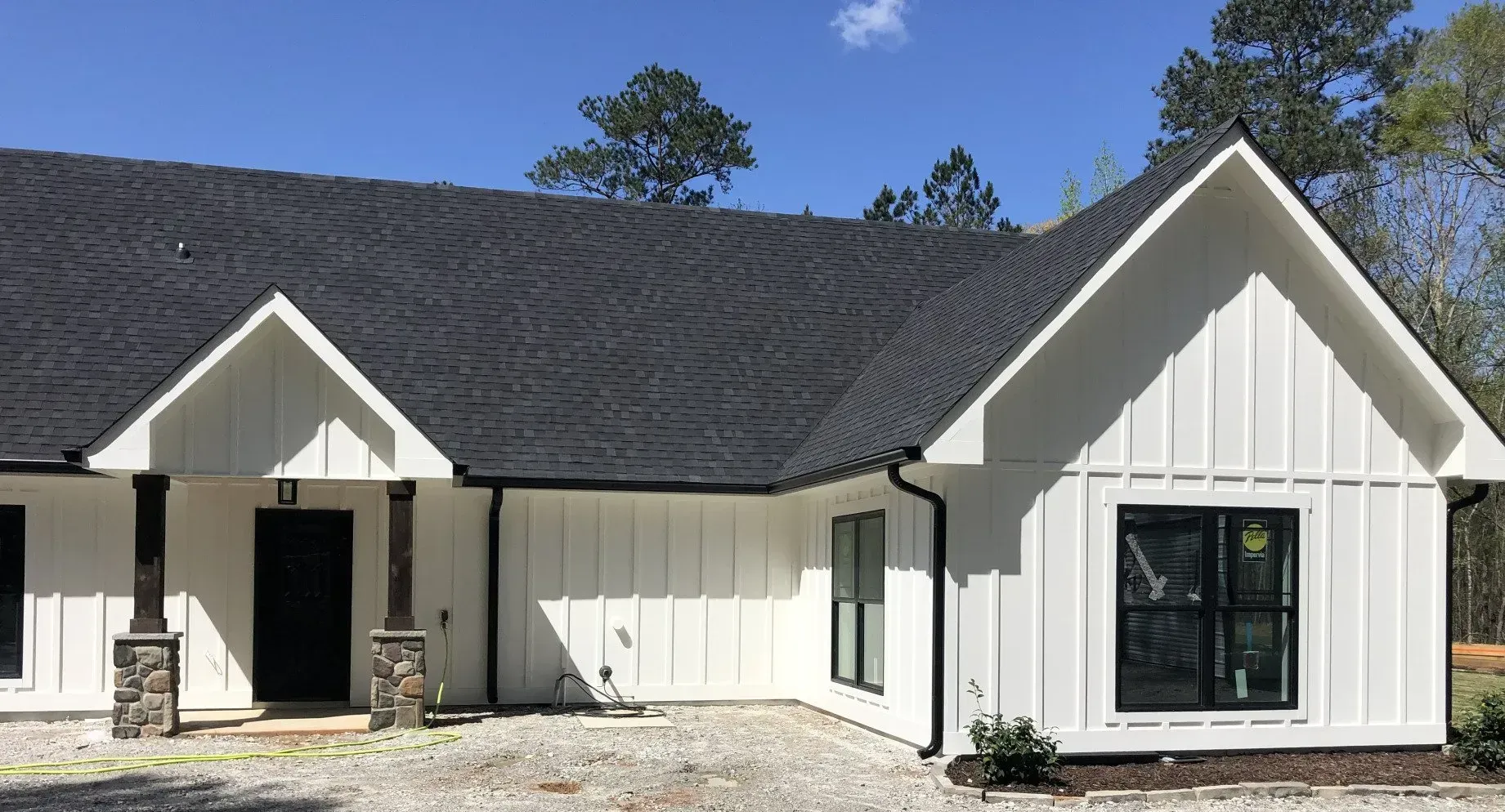White farmhouse with black roof and trim against a blue sky.