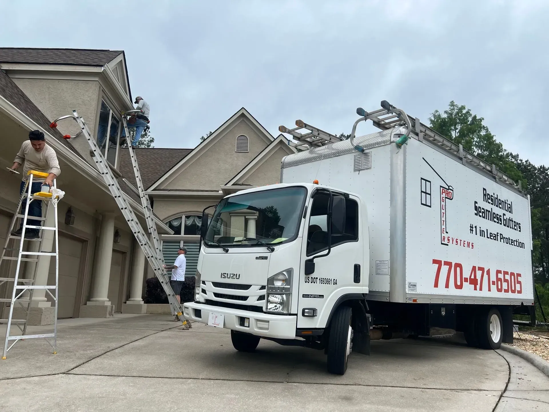 Truck parked in front of a house. Workers on ladders are repairing the roof and siding.