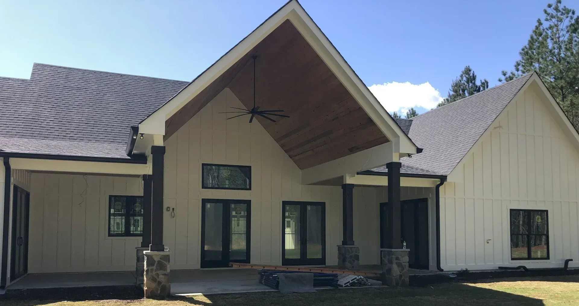 White farmhouse with black trim, covered porch, and brown wooden ceiling.