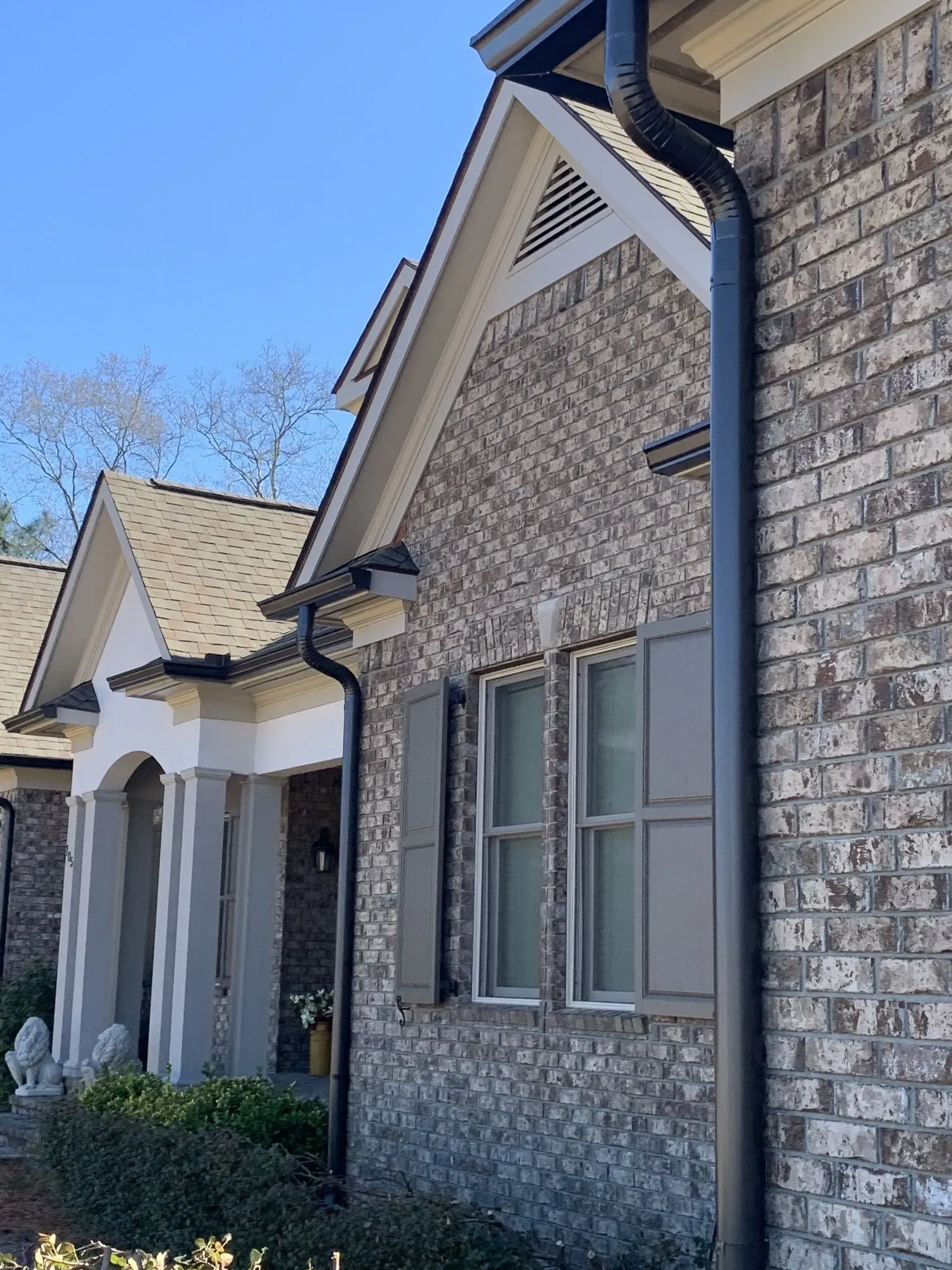 Brick house exterior with black gutters and downspout, gray shutters, and tan roof.