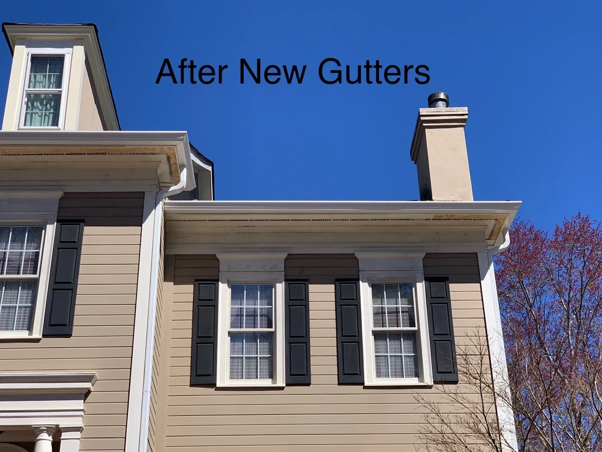 A tan house with new white gutters under a blue sky.