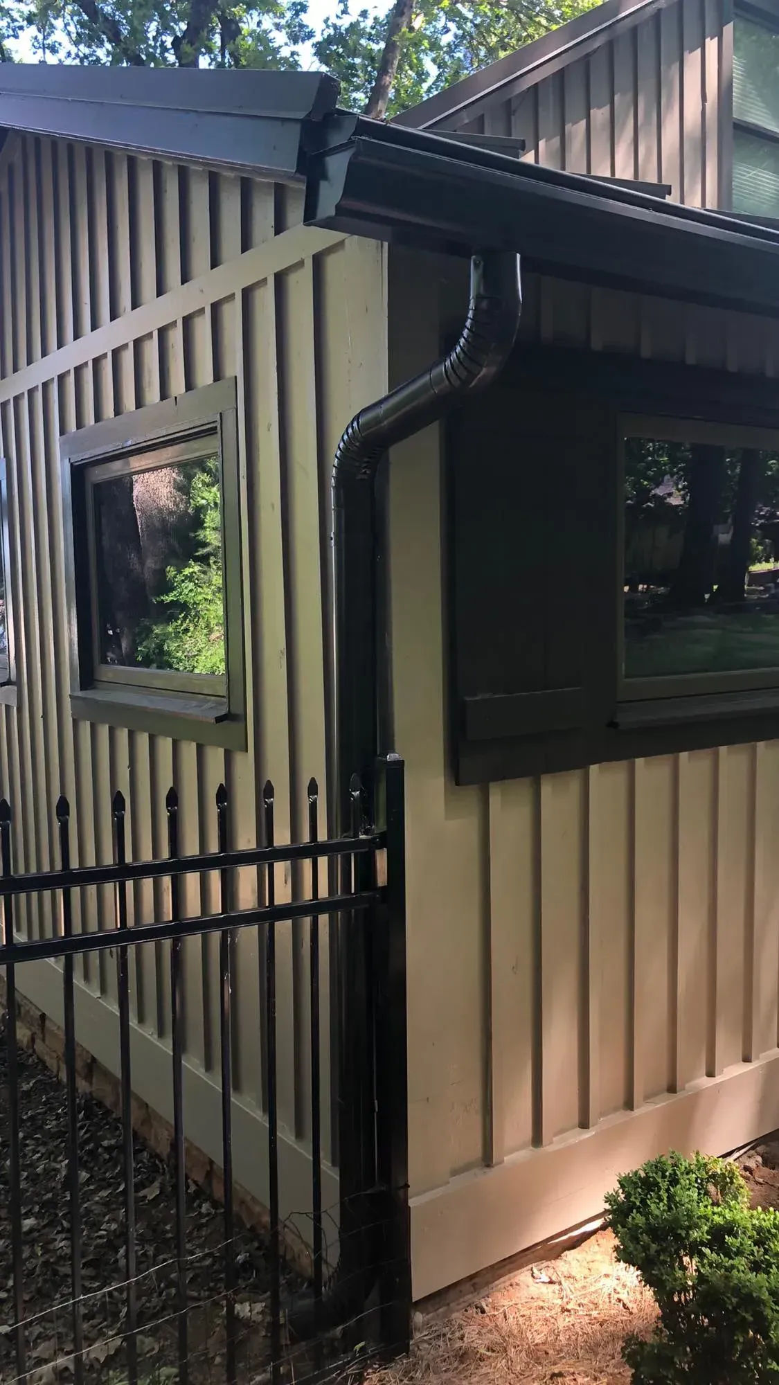 Exterior of a building with light brown vertical siding, black trim, and a black gutter.