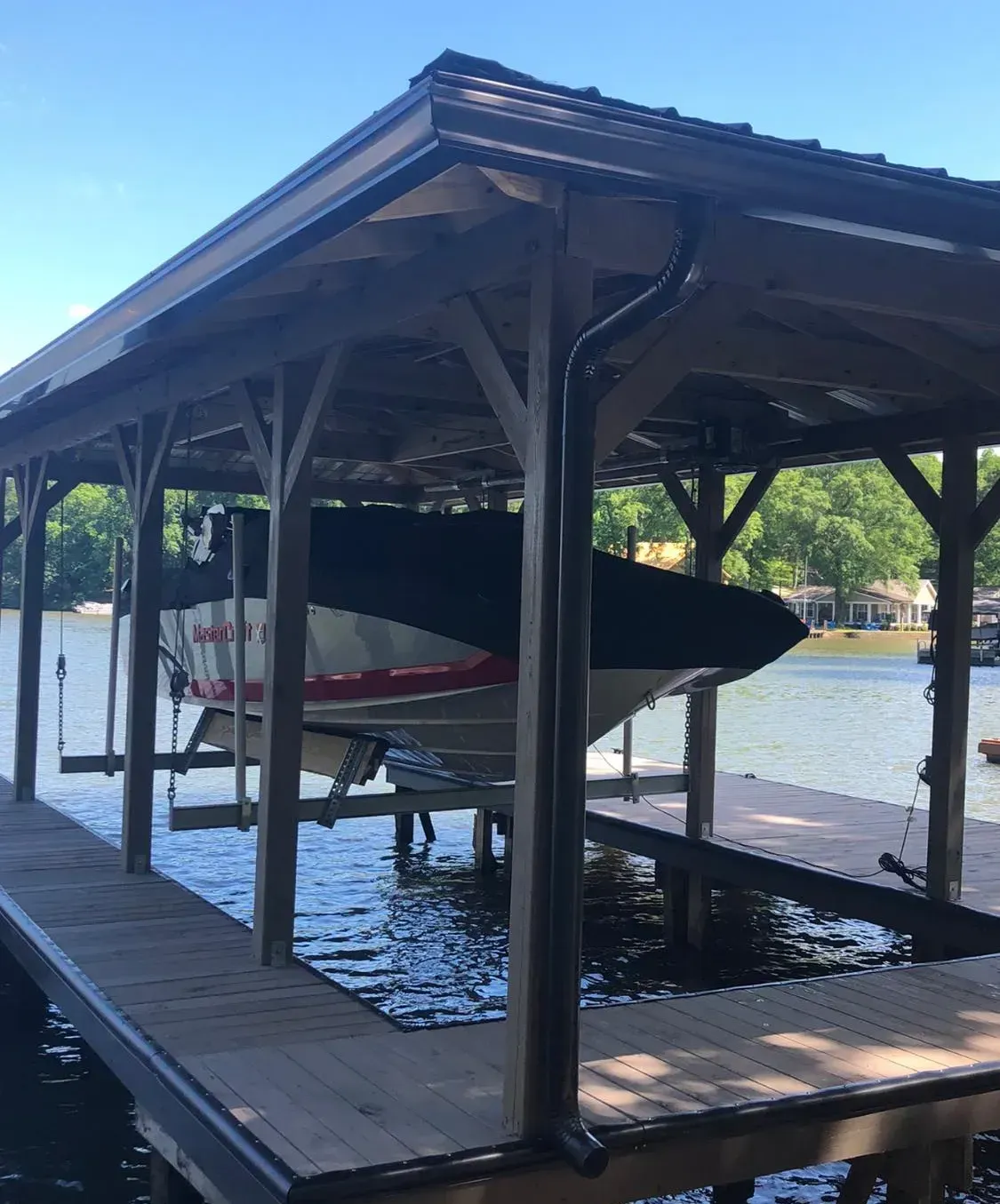 Boat covered under a wooden boat house on a lake, water, and trees in background.