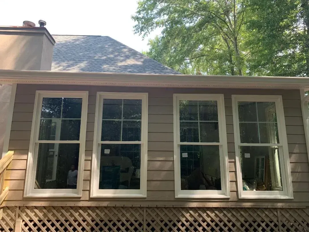 Four white-framed windows on a light-colored building with a dark roof and surrounding trees.