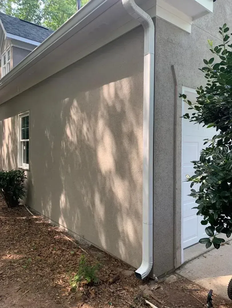 Tan stucco exterior of a building with white trim, a gutter, and a closed garage door.
