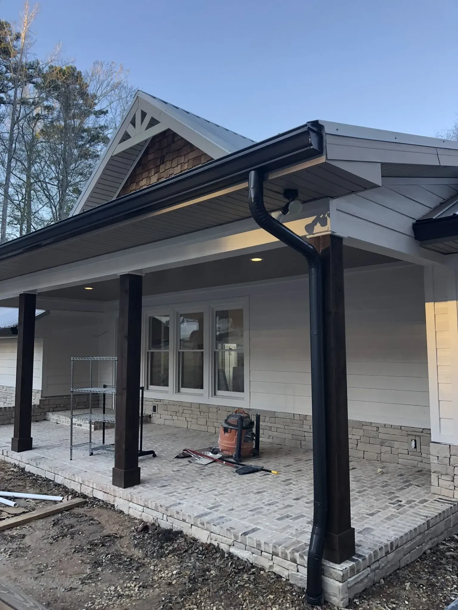 A house under construction with a black gutter, white siding, and brown support beams.