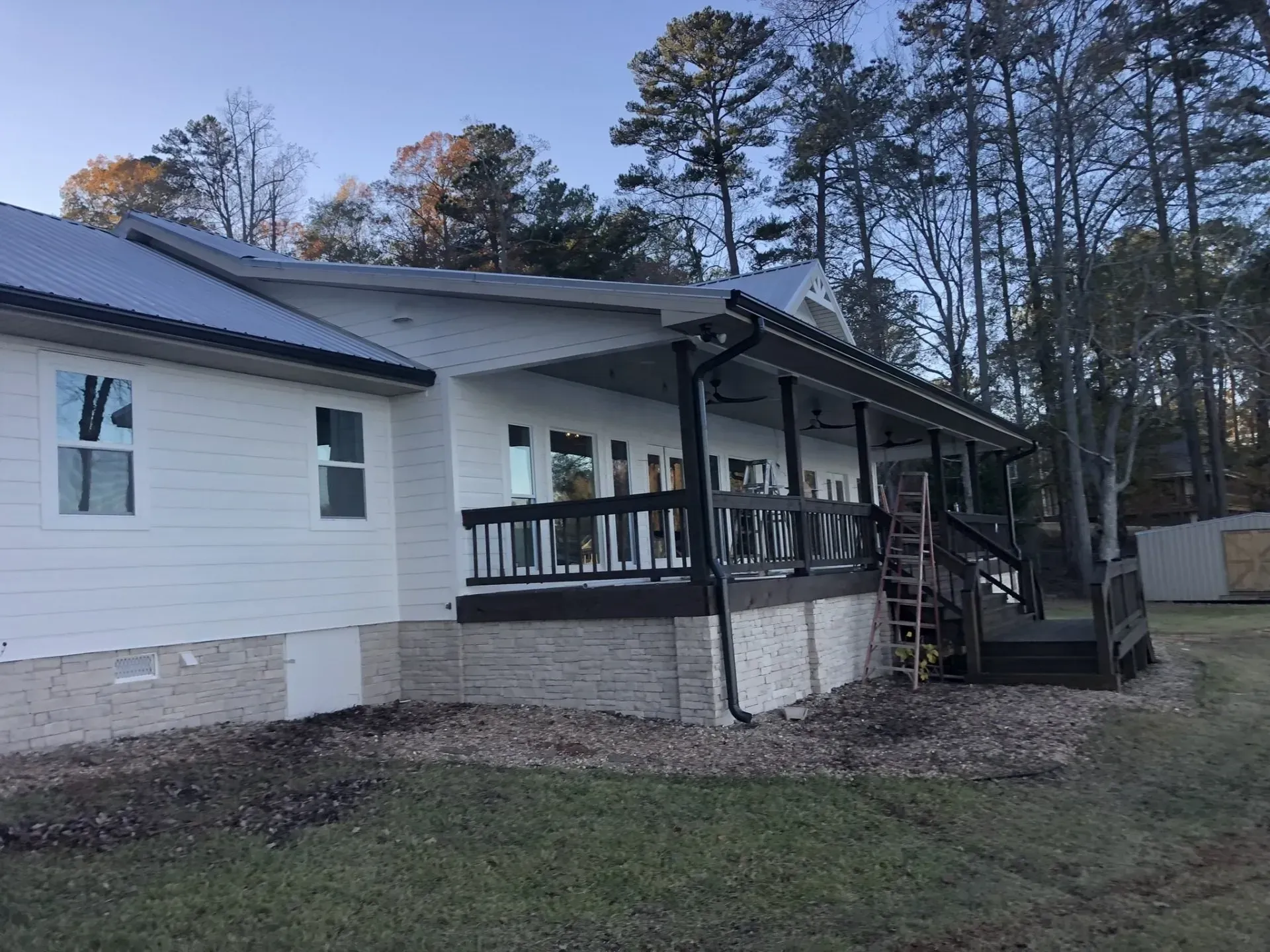 White house with a gray metal roof and black porch railing. Gravel and grass in the yard.