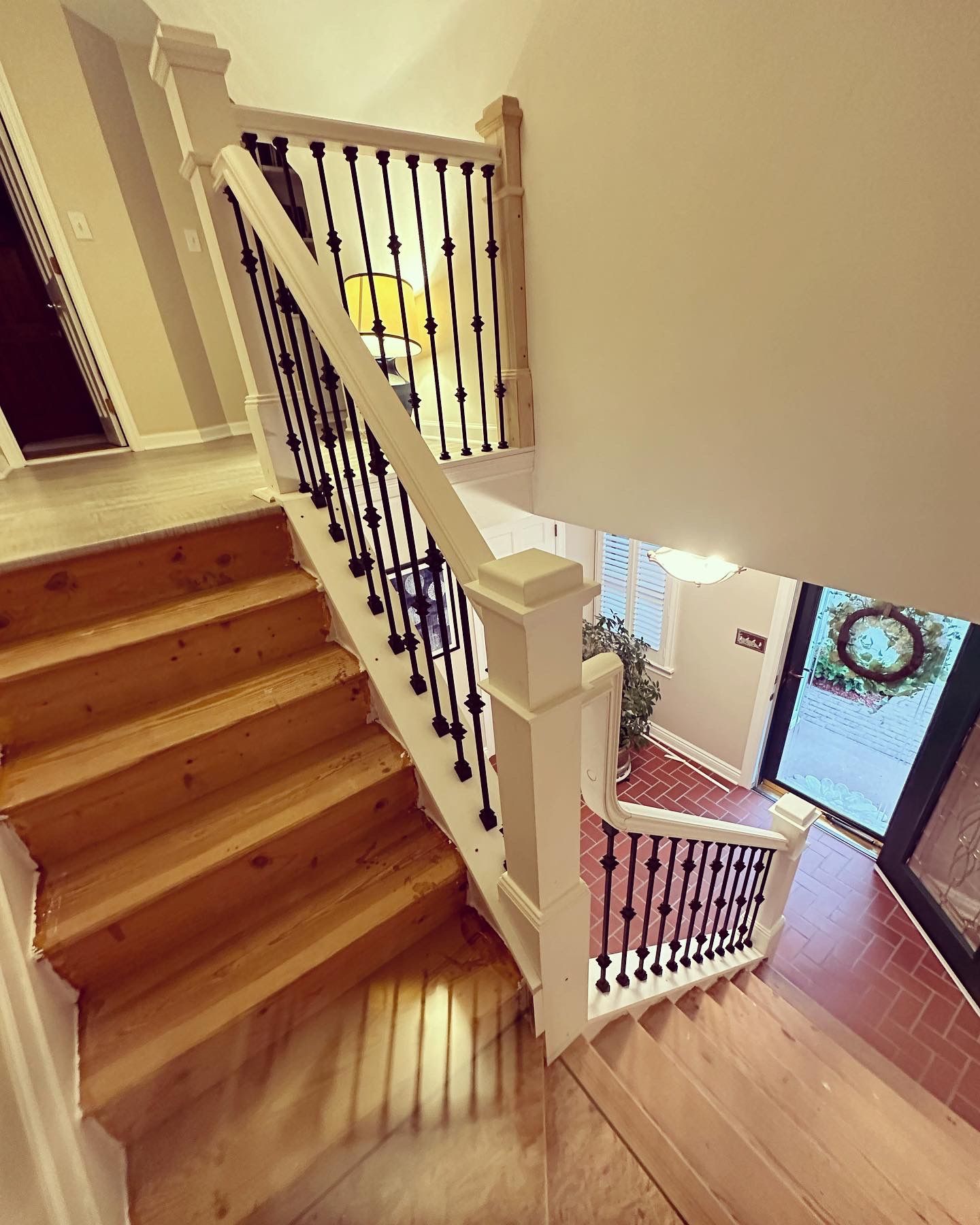 Wooden staircase with white railing, black spindles, leading down to entryway.