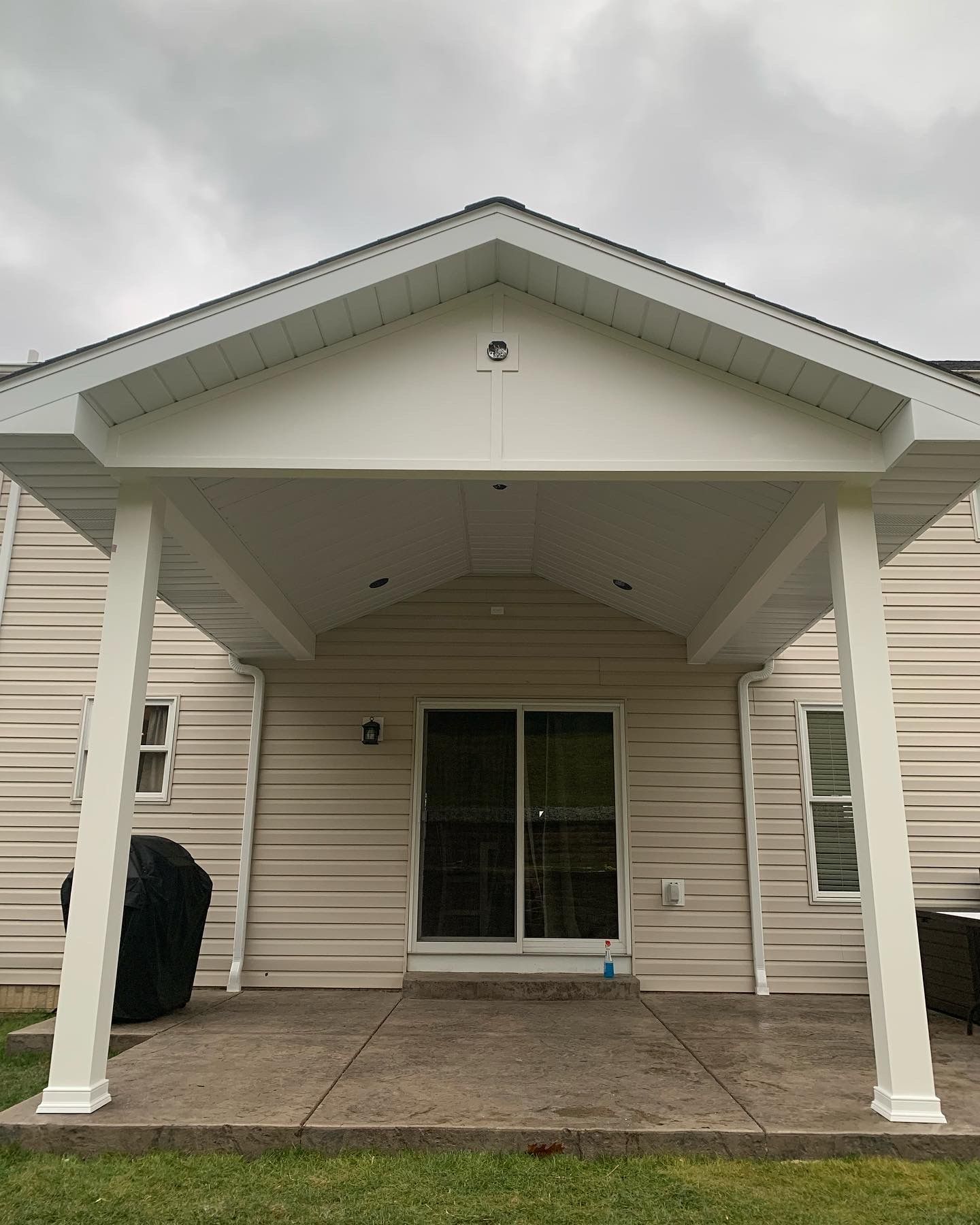 A white covered patio with two columns in front of a beige house, sliding glass door, on concrete.