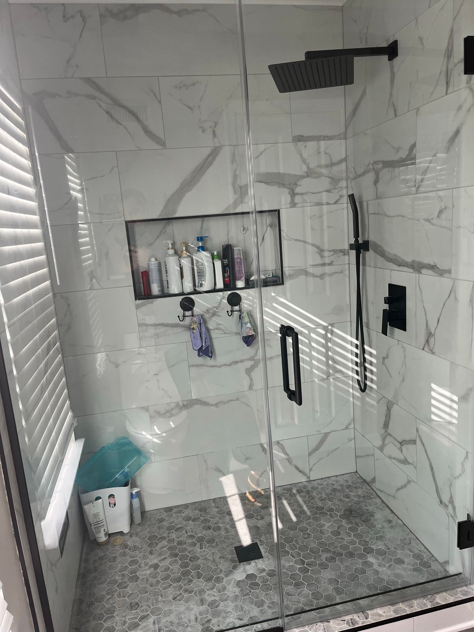 Modern shower with white marble tile, black fixtures, and a glass door.