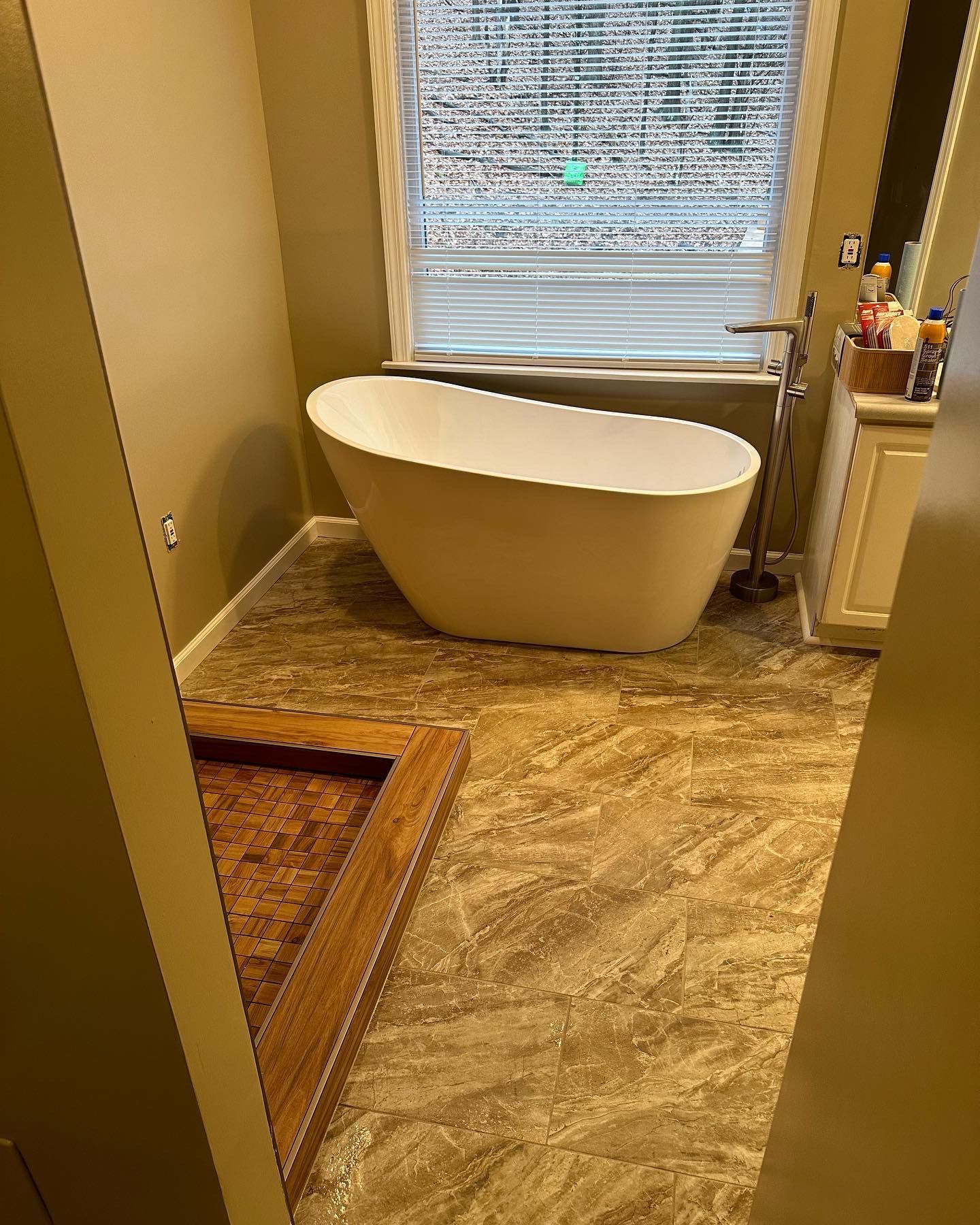 Bathroom with a freestanding white tub and beige-patterned flooring near a window and vanity.