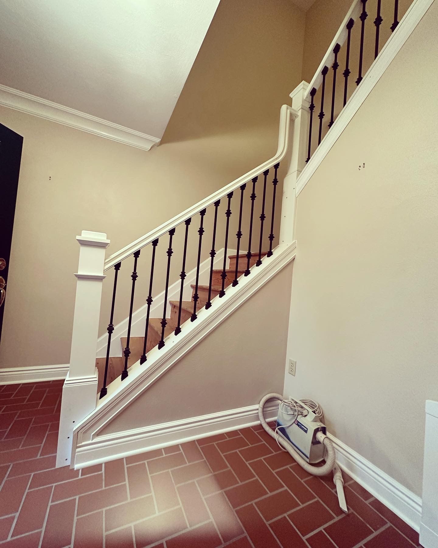 Interior view of a stairway with brick flooring, white trim, and black railings against beige walls.