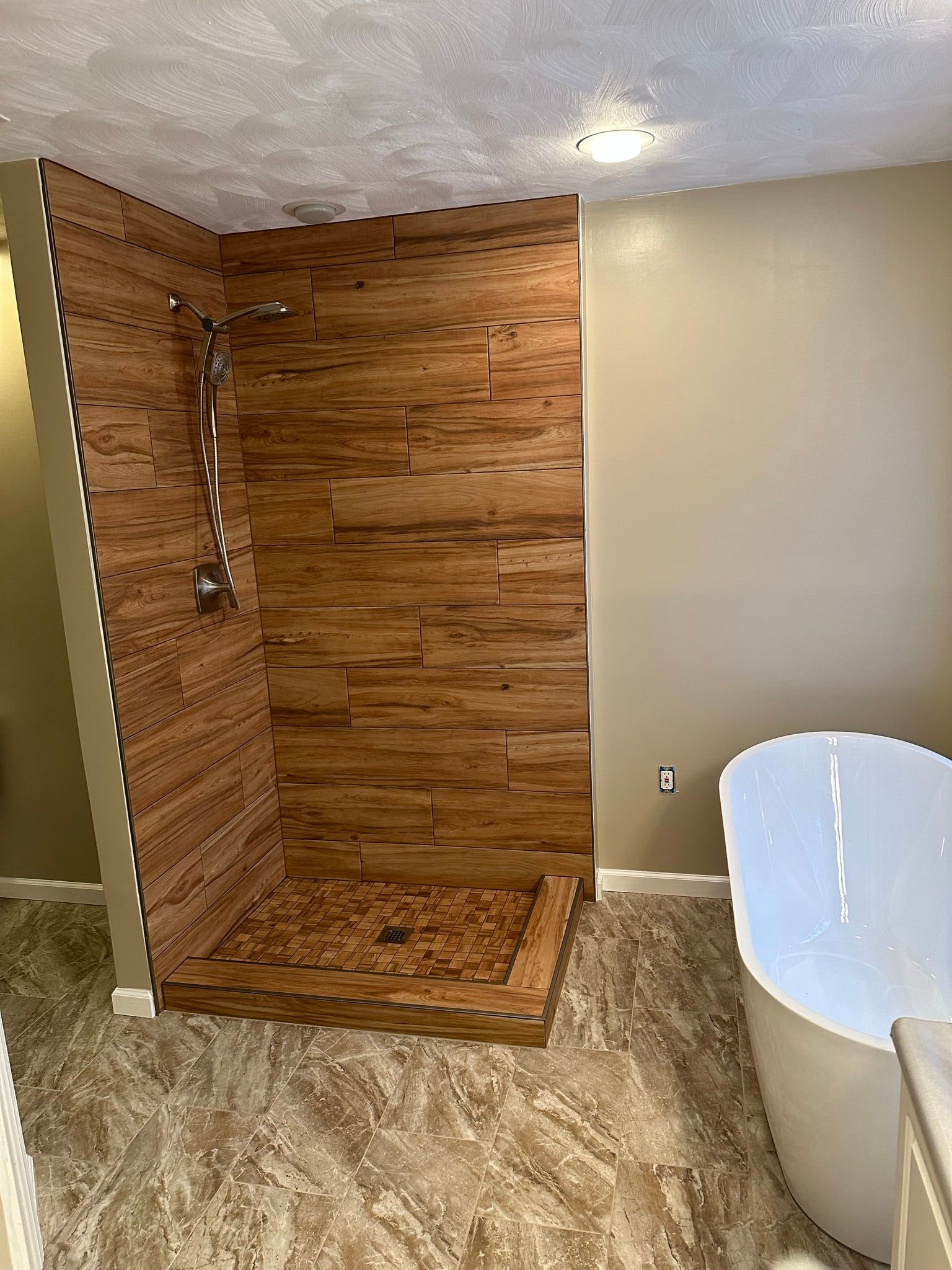 Wooden-tiled shower with rain shower head, light beige walls, and white bathtub on stone-look flooring.
